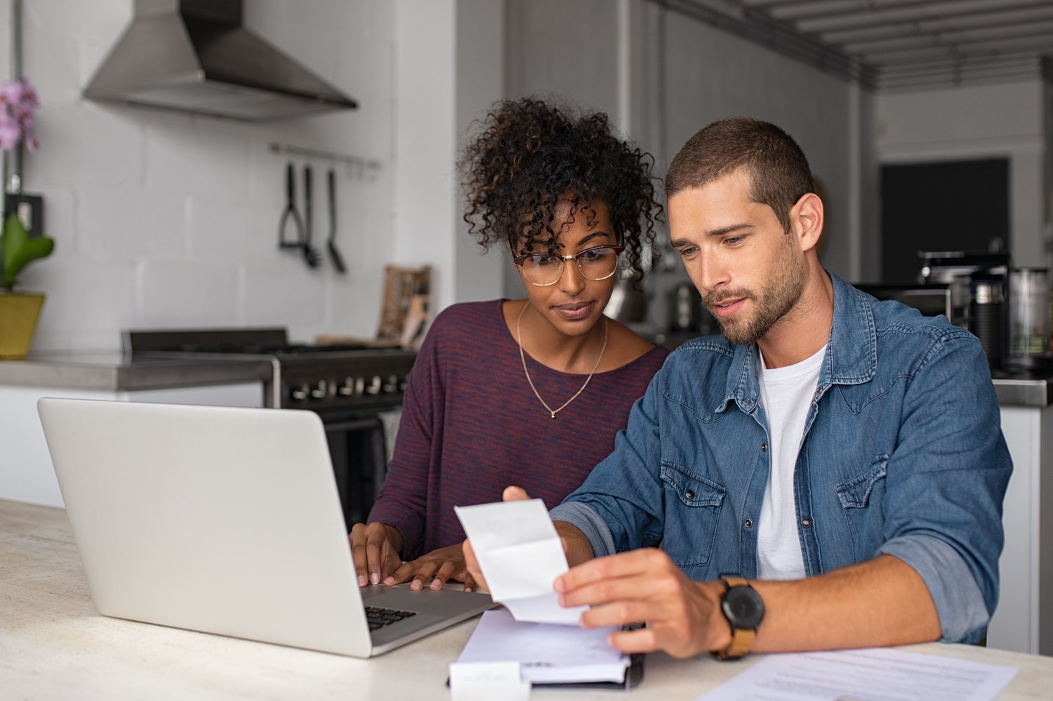 a young couple looks at receipts and a lap top as they budget for a project